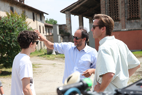 A man in a light blue shirt reaches out toward a young man in a white t-shirt while another man watches.