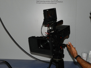 Professional video camera with a mounted monitor and a hand adjusting a knob.