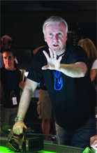 A man in a black t-shirt leans forward with one hand outstretched toward the viewer.