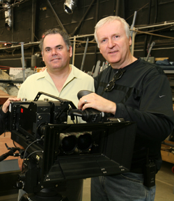 Two men posing behind a large professional motion picture camera in a studio setting.