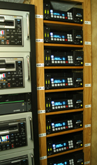 A wooden rack containing multiple rows of black electronic devices with digital displays and buttons.
