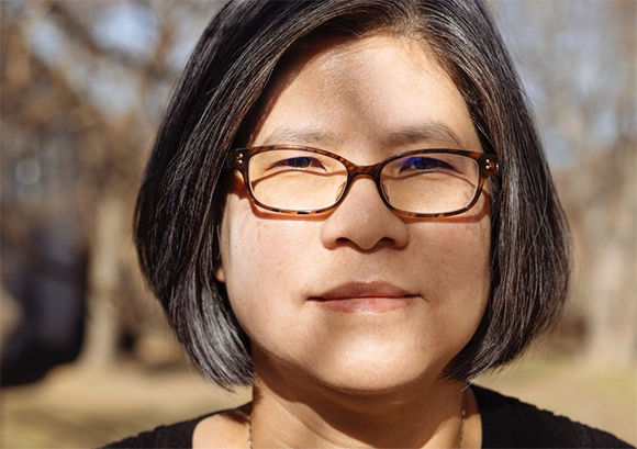Close-up portrait of a person with short grey hair and tortoiseshell glasses looking forward.