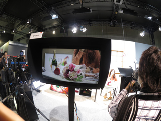 A person looks at a monitor displaying a close-up of champagne and flowers in a studio.
