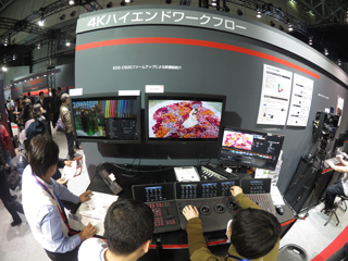 People viewing professional 4K video editing monitors and control consoles at a technology exhibition.