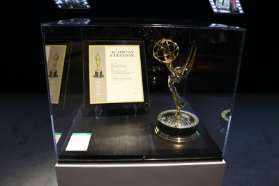 An Emmy award trophy and an Academy Citation document are displayed in a glass case.