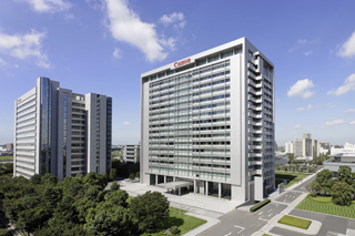Two tall, modern glass and steel office buildings standing near green trees under a blue sky with clouds.