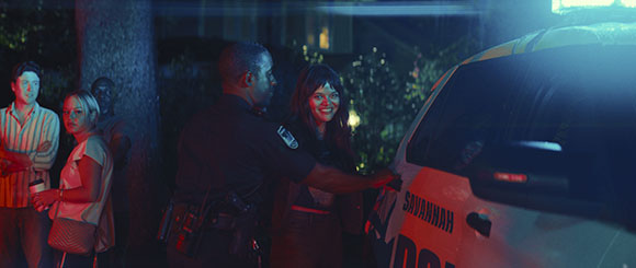 A police officer talks to a smiling woman next to a Savannah police vehicle at night.