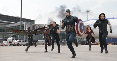 Several superheroes in costume run toward the camera on an airport tarmac.
