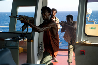Three men on a boat deck; one man in the foreground aims a rifle toward the left.