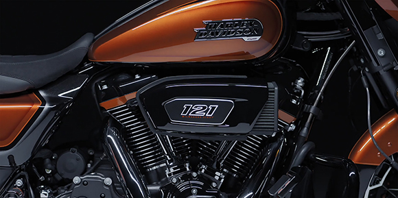 Close-up of an orange Harley-Davidson fuel tank and a black engine with a 121 Milwaukee-Eight badge.