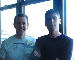 Two men standing side by side in front of a bright window.