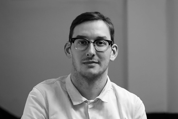 Black and white portrait of a man with short hair and glasses wearing a light-colored polo shirt.
