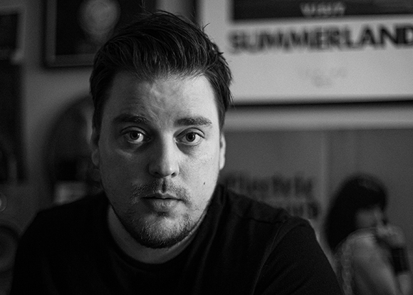 Black and white close-up portrait of a man with dark hair and light facial hair looking forward.
