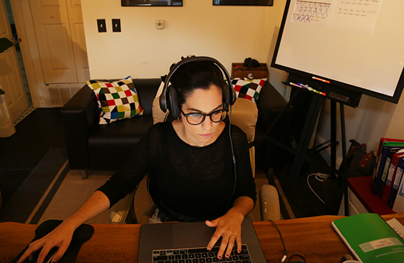 A woman with glasses and headphones uses a laptop and mouse at a wooden desk in a home office.