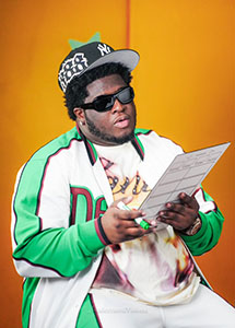 A man wearing a baseball cap, sunglasses, and a green and white jacket holds a clipboard.