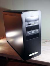 A black vertical desktop computer tower sitting on a light-colored wooden table.