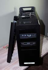 A black desktop computer tower standing on a table with its side panel detached and leaning against it.