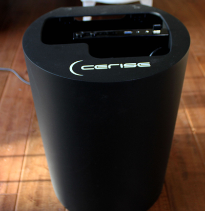 A black cylindrical Cerise device sitting on a wooden floor with an open top compartment.