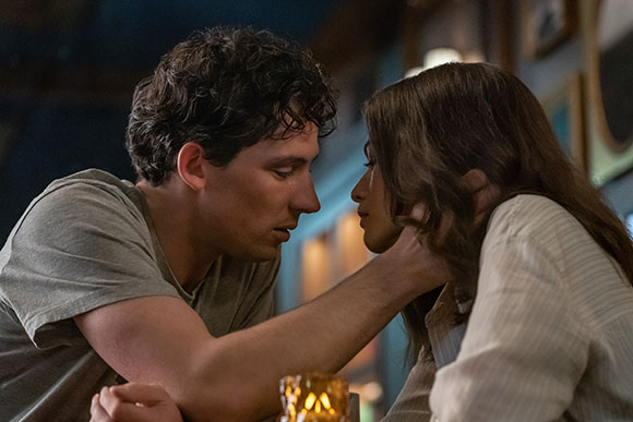A man leans toward a woman, holding her chin as they look into each other's eyes.