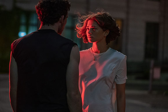 A man in a black tank top faces a woman in a white t-shirt under dim red and blue light at night.