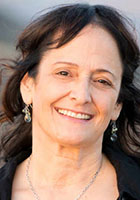 A smiling woman with dark hair and dangling earrings looks toward the camera.