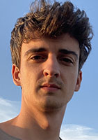 A young man with wavy brown hair looking forward against a clear blue sky.