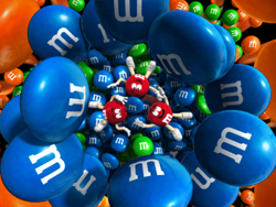 A pile of blue, orange, and green M&M's candies with three red M&M's characters in the center.