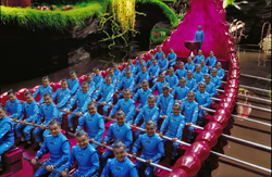 A large group of people in matching blue uniforms sitting in rows inside a long, bright pink vessel.