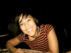 A smiling woman with short dark hair wearing a red and black striped shirt.