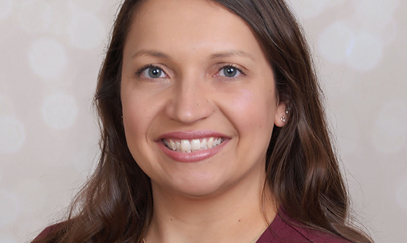 A smiling woman with long brown hair and blue eyes looking at the camera.