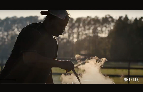 A person in silhouette cooking over a steaming pan outdoors during sunset.