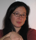 A woman with long dark hair and black-rimmed glasses looking forward.