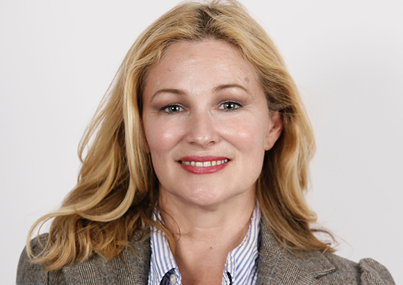 A blonde woman with blue eyes and a slight smile looking directly at the camera.