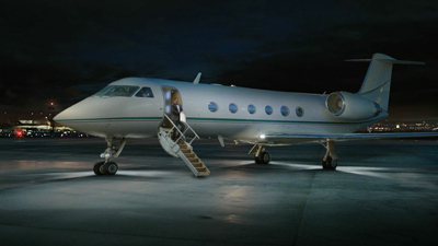 A white private jet on a dark airport tarmac with its boarding stairs extended.