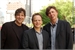 Three men in dark blazers and button-down shirts smiling for a portrait outdoors.