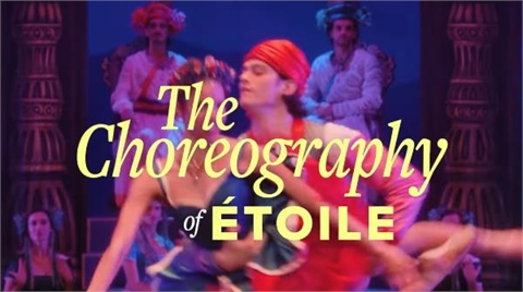 Dancers in colorful theatrical costumes perform on a stage with large decorative pillars.