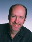 A smiling man with thinning hair and a light beard wearing a dark collared shirt.