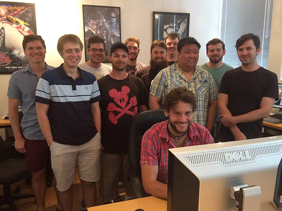 A group of eleven men standing together in an office with movie posters on the wall.