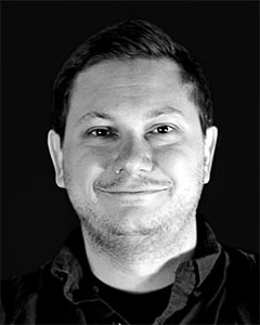 A man with short hair and stubble smiles directly at the camera in a black and white headshot.