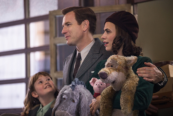 A man and woman smile while holding a large brown teddy bear and a grey stuffed animal.