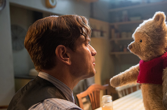 A man in profile stares closely at a small teddy bear wearing a red shirt.