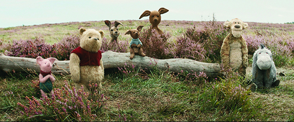 Stuffed animal characters sit in a grassy field with purple flowers and a fallen log.