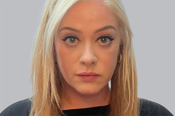 Close-up portrait of a blonde woman with light eyes, winged eyeliner, and a small nose ring.