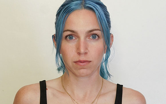 A woman with blue hair and blue eyes looking forward against a plain white background.