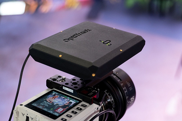 A black OptiTrack sensor device mounted on a white professional camera with a lens.