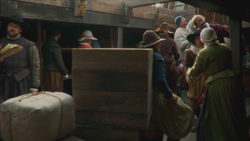 Several people in period clothing move large wooden crates and heavy sacks in a rustic setting.