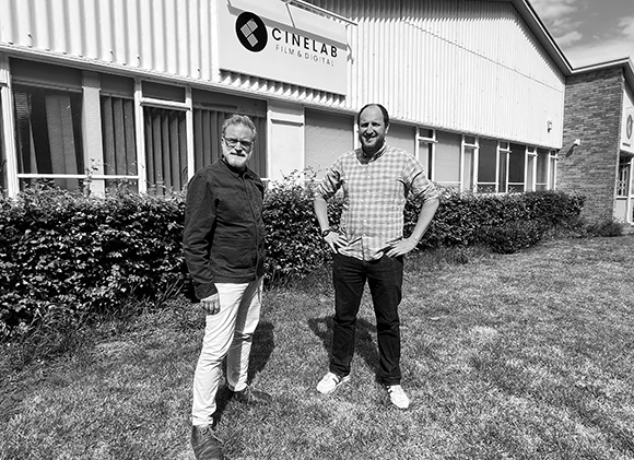 Two men standing on a lawn in front of a Cinelab Film & Digital building.