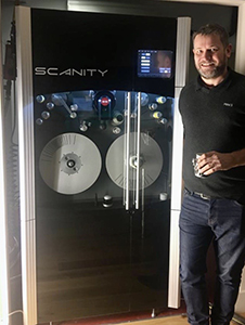A man smiling while standing beside a large black Scanity film scanning machine.