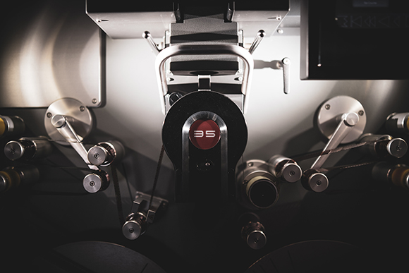 Close-up of complex industrial machinery with metal gears, belts, and a central red circular emblem.
