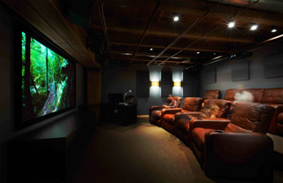 A dark home cinema with a large screen displaying a forest and rows of brown leather reclining seats.